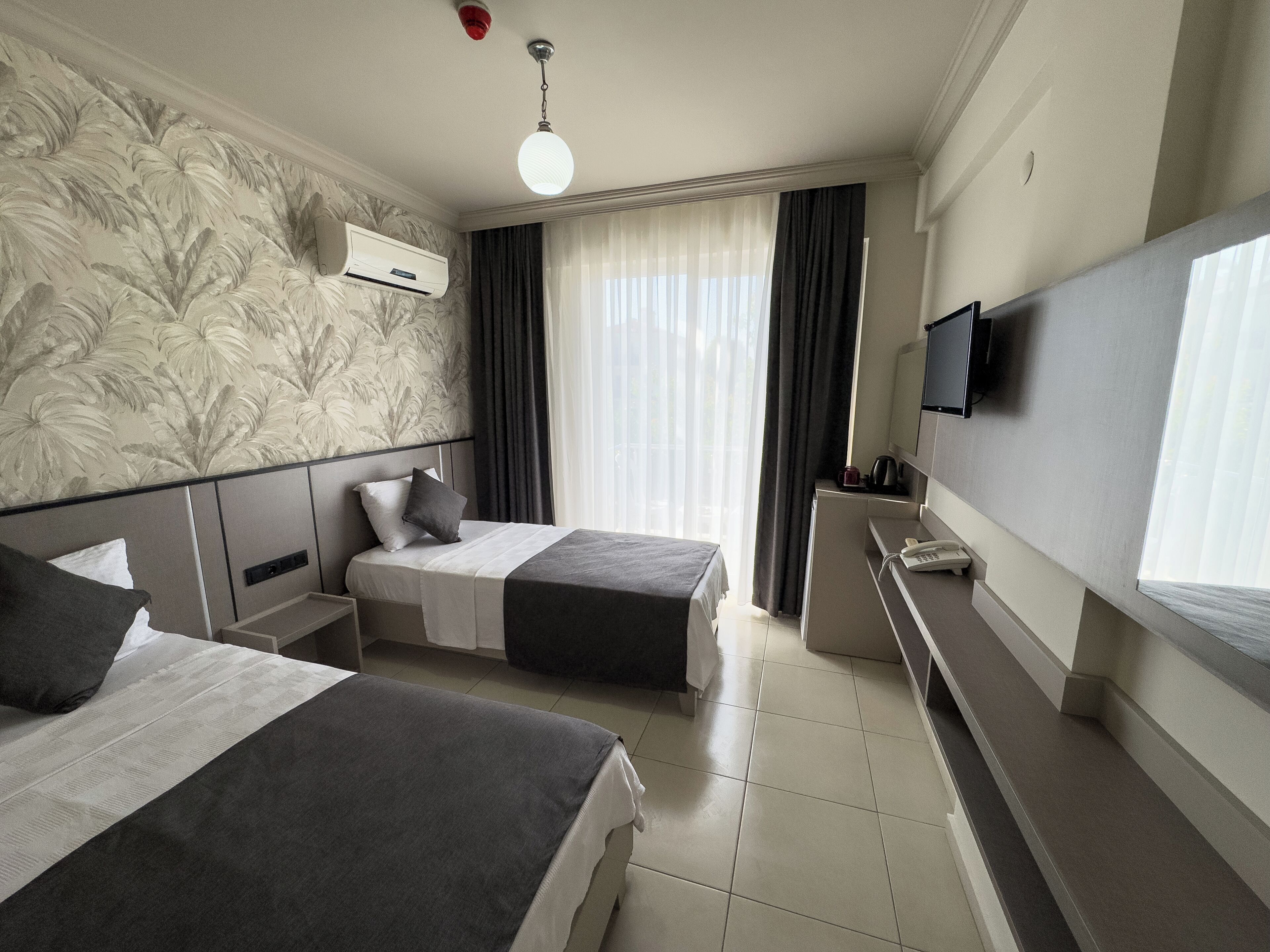 A hotel room with two beds, a TV, an air conditioning unit, and a window with curtains.