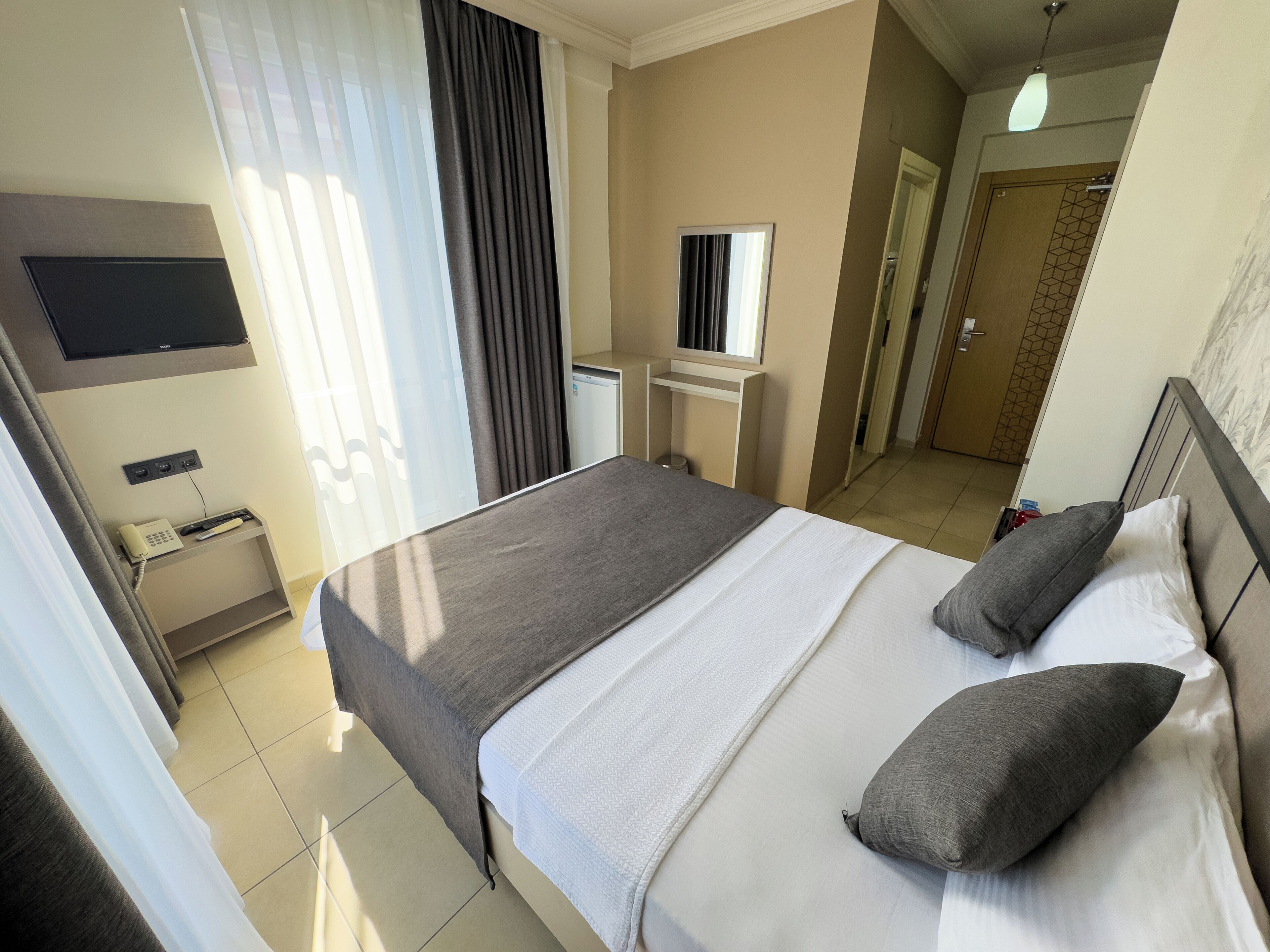 Une chambre d’hôtel avec un lit, un téléviseur fixé au mur, un bureau avec un téléphone et un miroir.