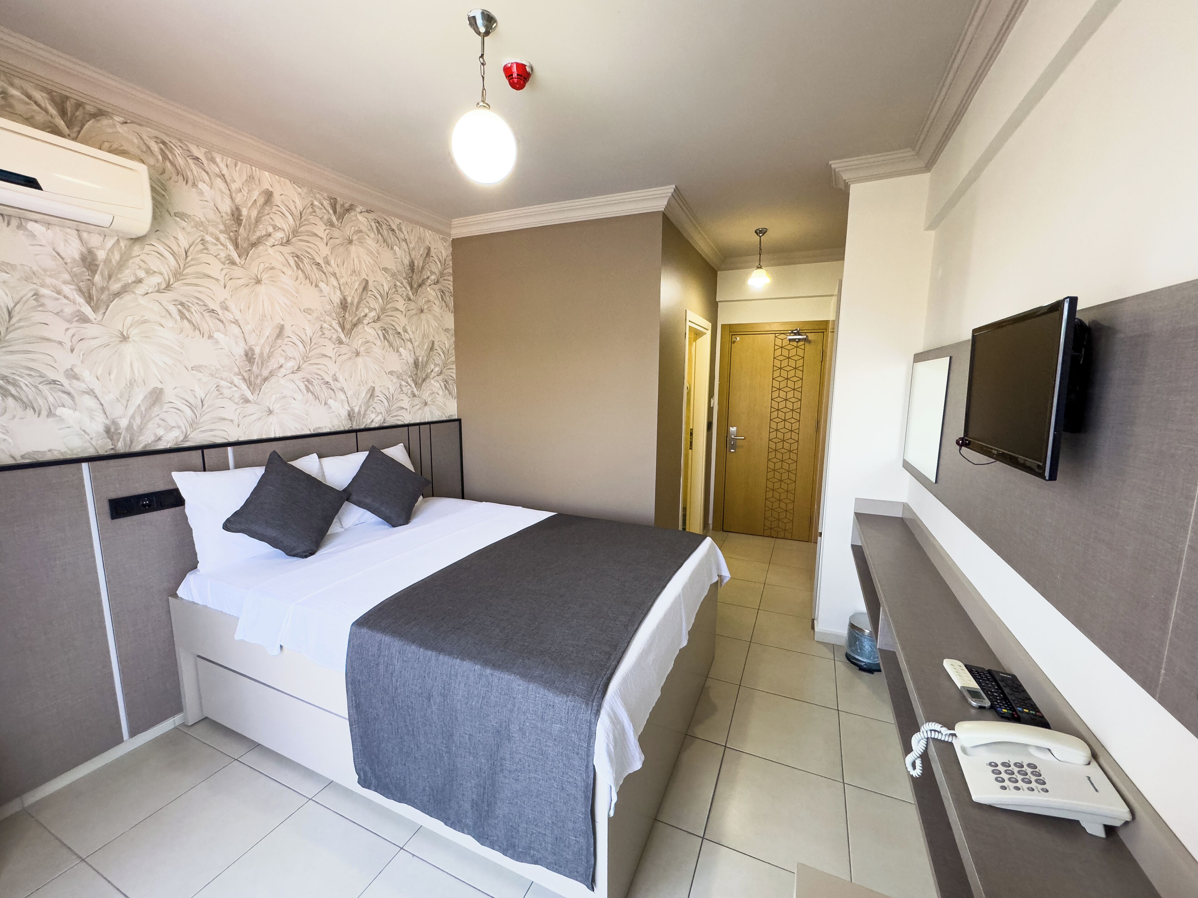 Une chambre d’hôtel équipée d’un lit, d’un téléviseur fixé au mur, d’un téléphone et d’une porte donnant sur une autre pièce.