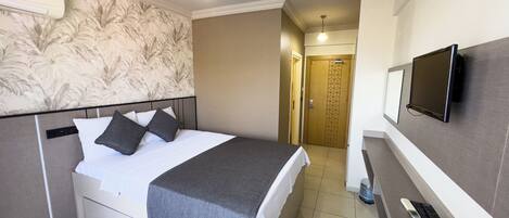 A hotel room with a bed, a TV mounted on the wall, a telephone, and a door leading to another room.