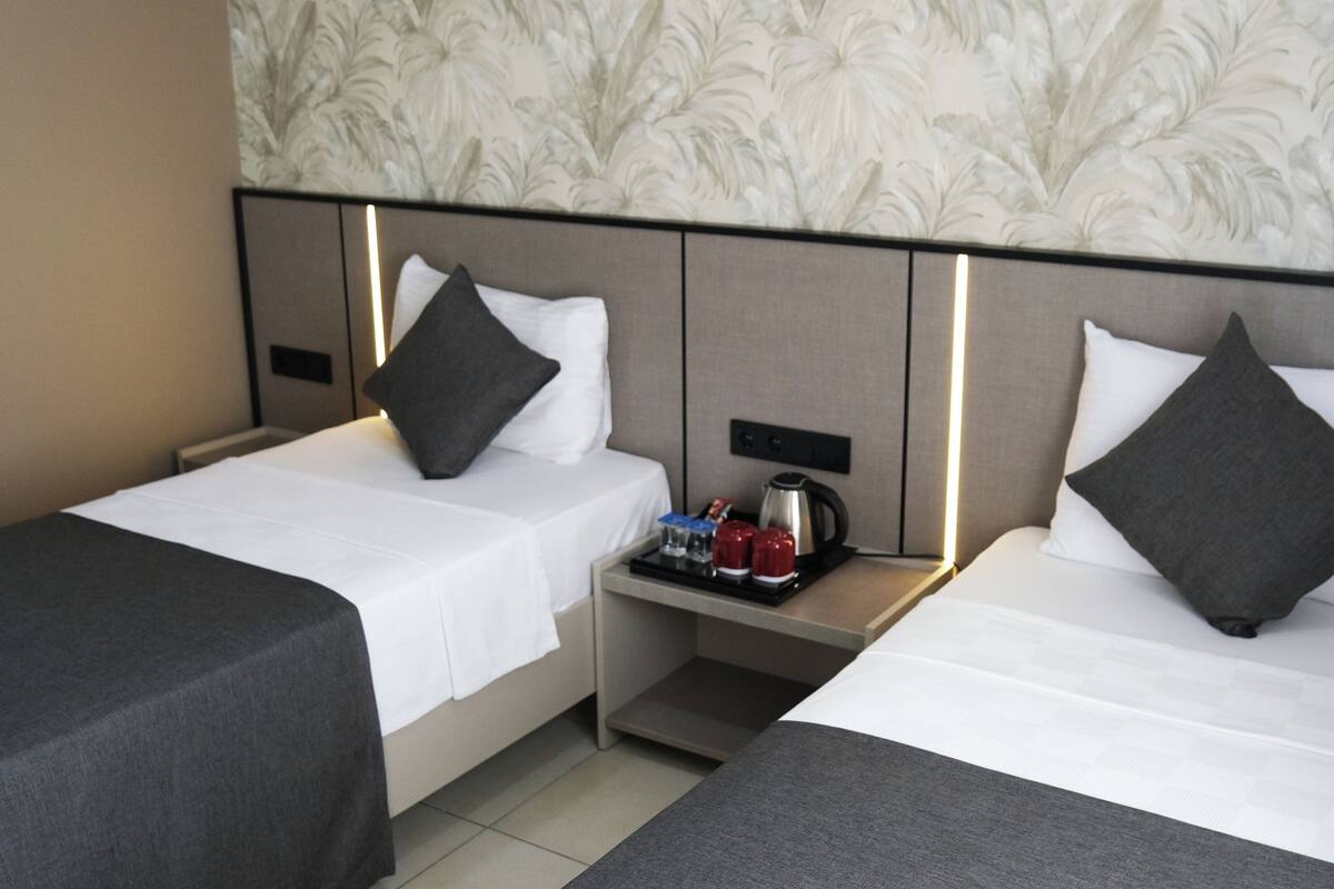 A hotel room with two single beds, each with a pillow and a bedside table with a kettle and glasses.