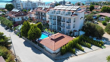 A multi-story hotel with a swimming pool, surrounded by lush greenery and a coastal view.