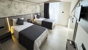 Ein Hotelzimmer mit zwei Betten, einem Fernseher, einem Schreibtisch und einem Fenster mit Vorhängen.