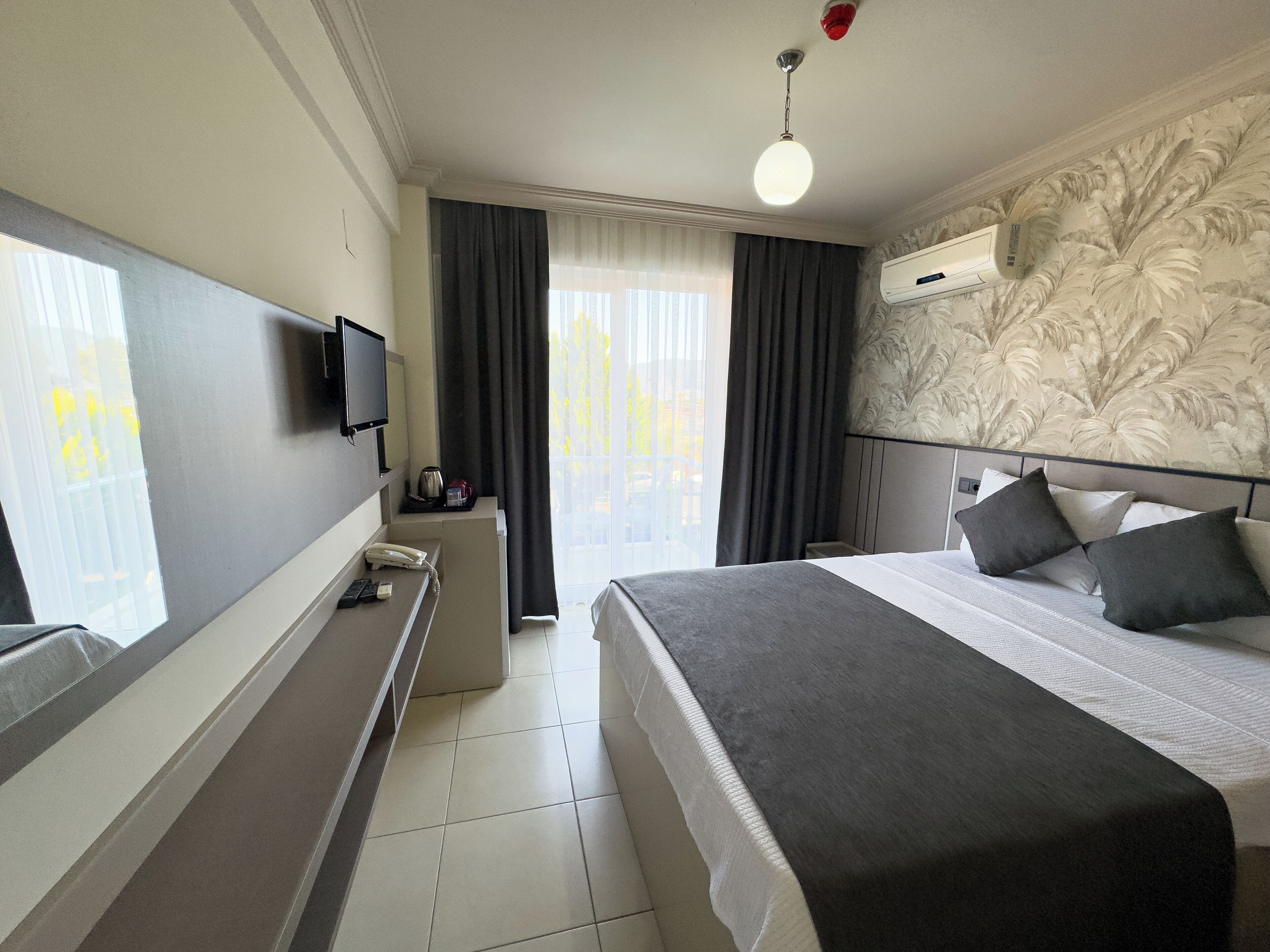 A hotel room with a bed, a television, a telephone, and a window with curtains.