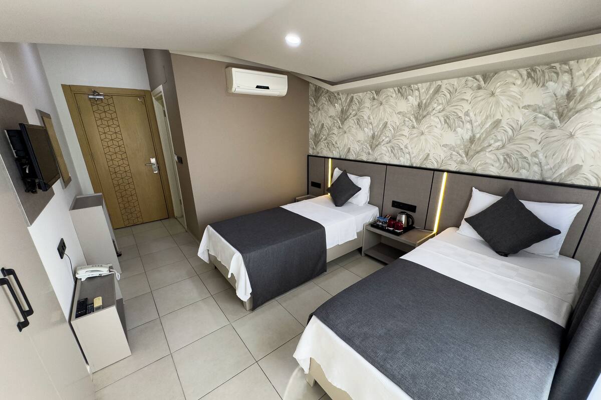 A hotel room with two beds, a desk, a telephone, and an air conditioning unit.