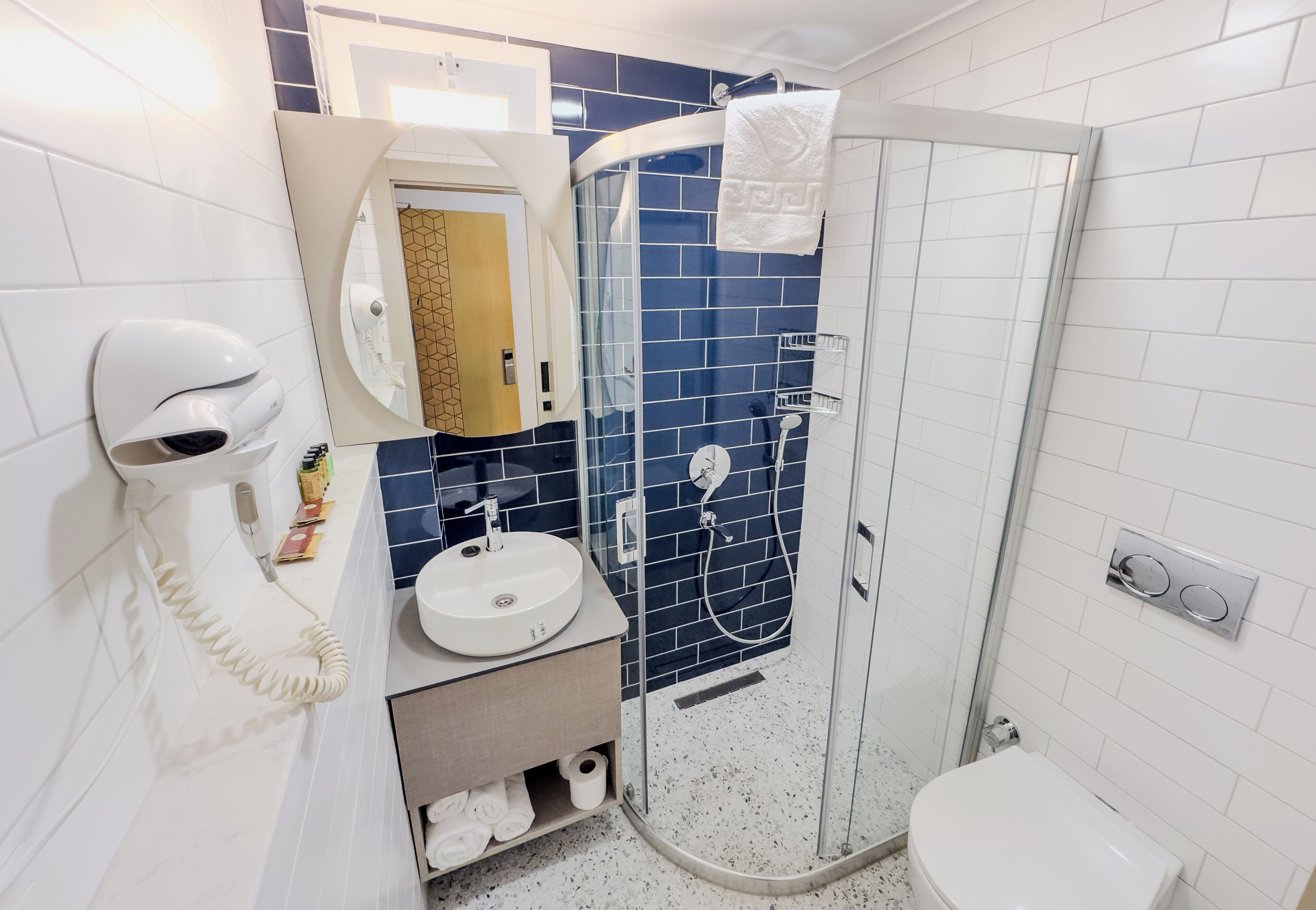 A bathroom with a glass-enclosed shower, a white sink, a hairdryer, and a towel rack.