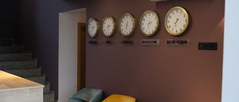 A room with a staircase, a reception desk, and five clocks labeled with city names.