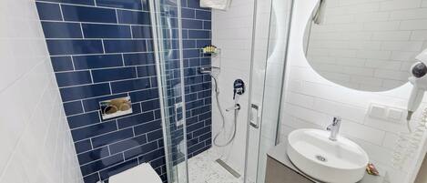 A bathroom with a glass shower enclosure, a white toilet, a sink with a mirror, and blue-tiled walls.