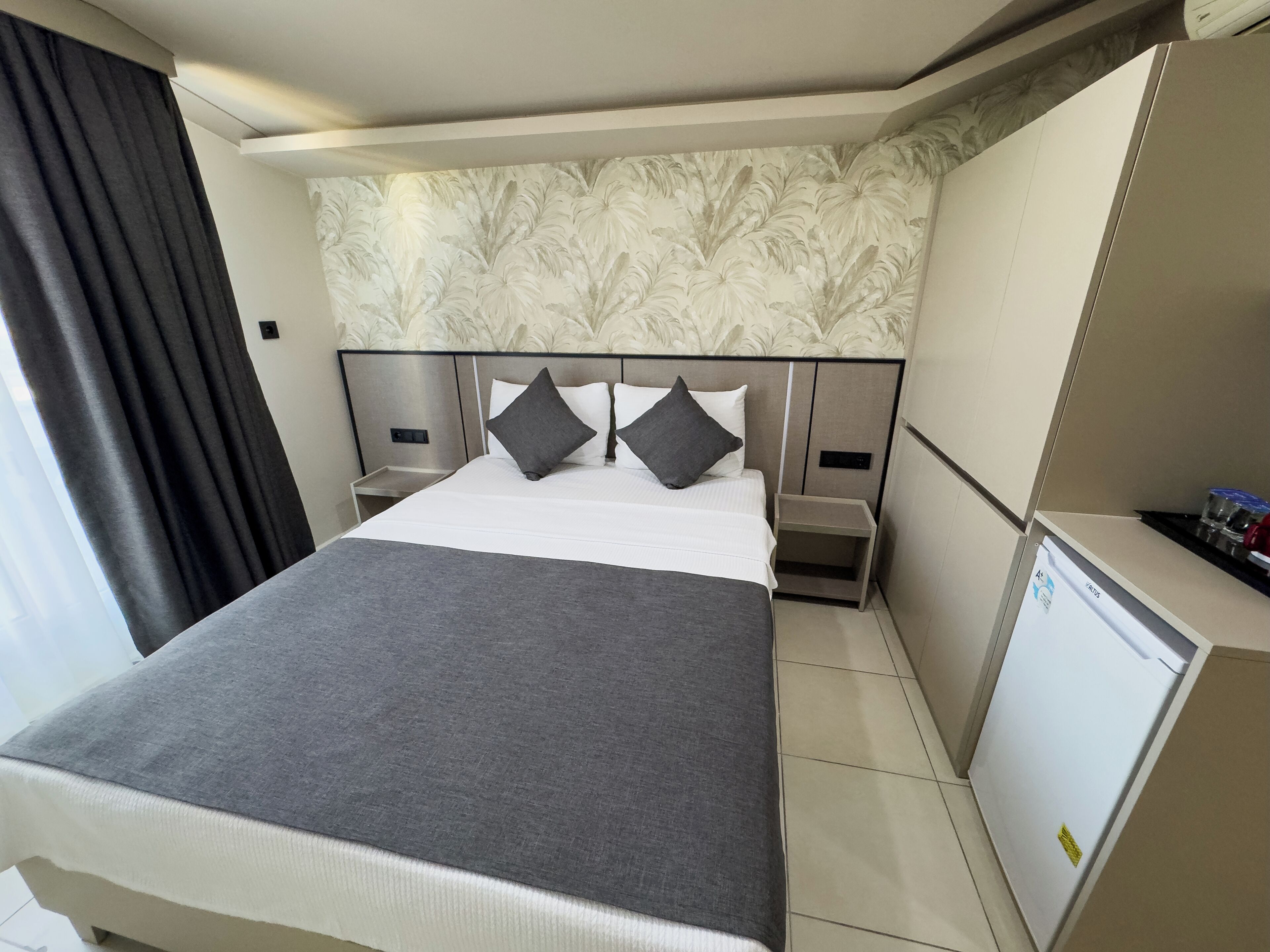 A hotel room with a large bed, two bedside tables, a small desk, and a refrigerator.