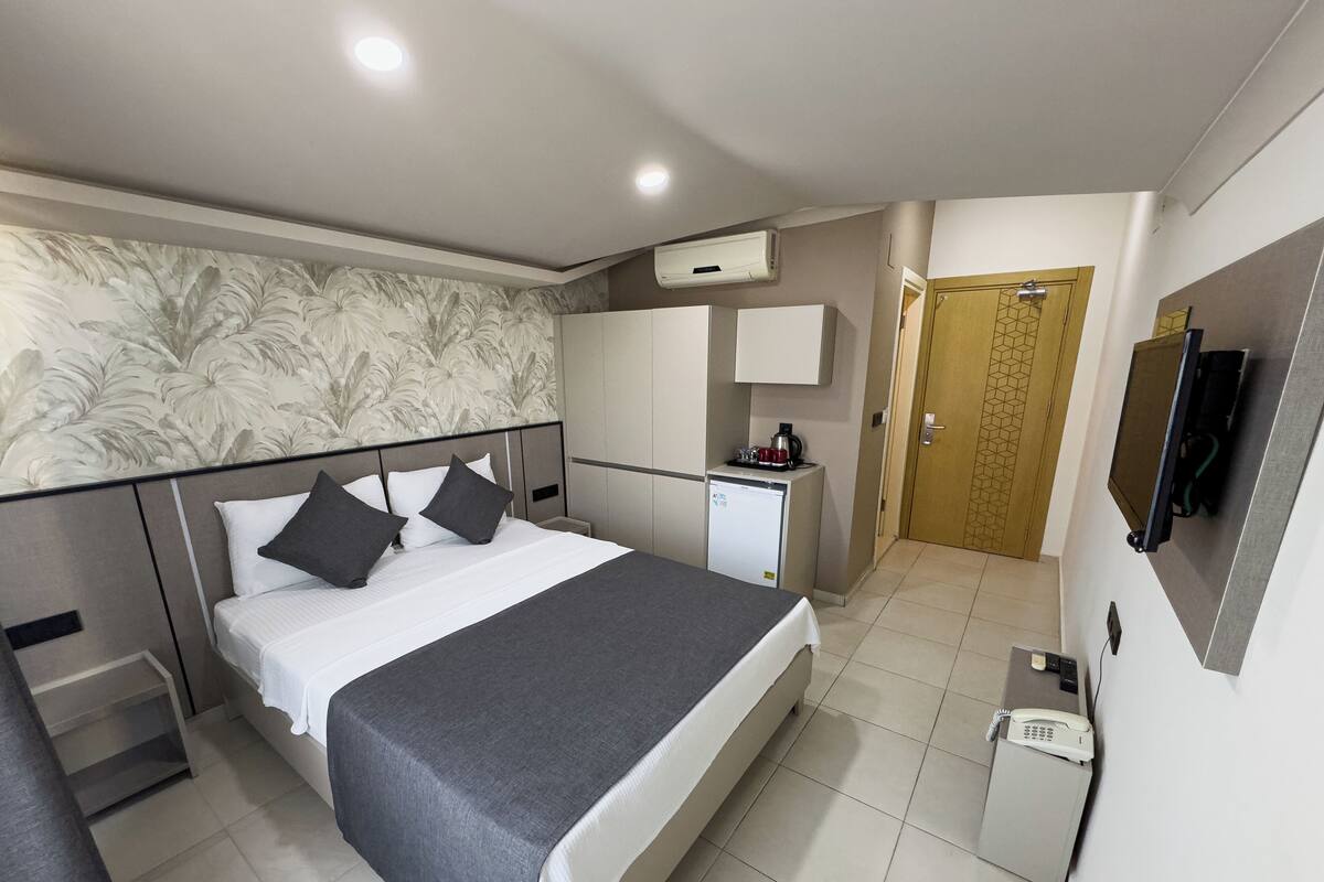 A hotel room with a bed, a desk, a minibar, a television, and an air conditioning unit.