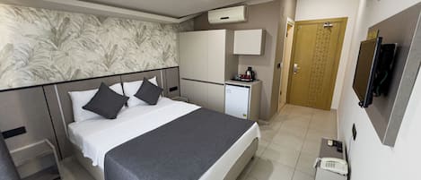A hotel room with a bed, a desk, a minibar, a television, and an air conditioning unit.
