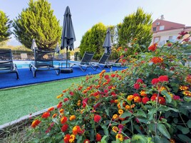 A pool area with lounge chairs and umbrellas, surrounded by vibrant flowers and trees.