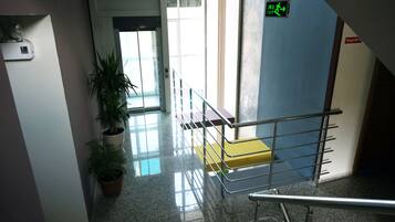 Um corredor com corrimão de metal, plantas em vasos, escada e sinal de saída.