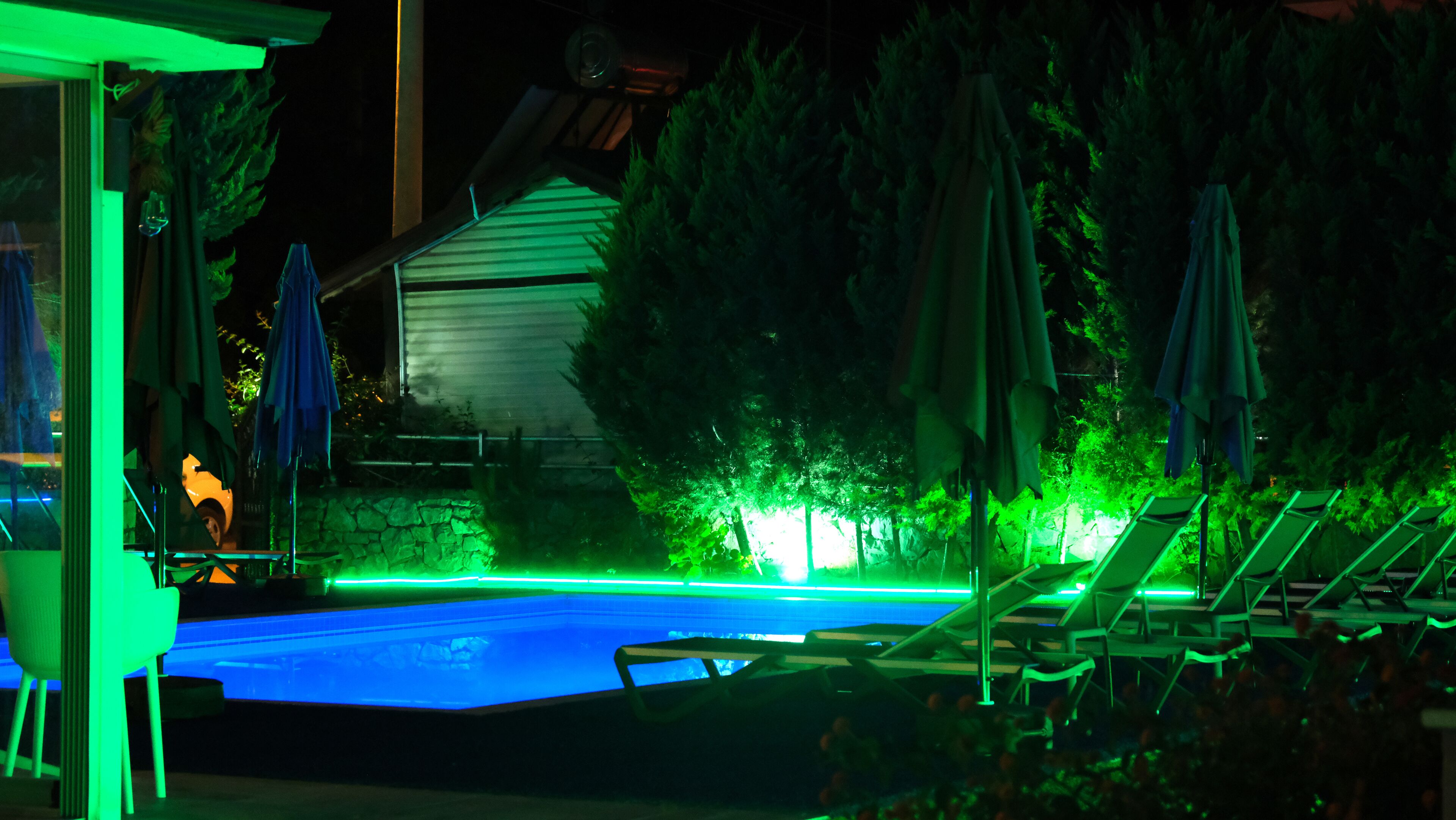 A swimming pool with green lighting, surrounded by lounge chairs and umbrellas.