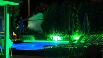A swimming pool with green lighting, surrounded by lounge chairs and umbrellas.