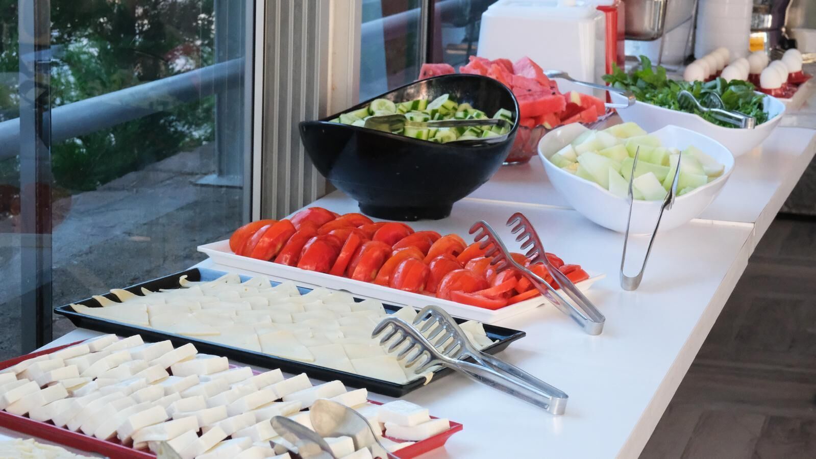 Una mesa de buffet con diversos alimentos, incluyendo rodajas de tomate, pepino y queso.