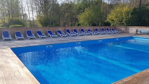 A swimming pool with blue water, surrounded by wooden deck and blue lounge chairs. - Camping Le Petit Lion - Lodges Bois (Vendoire)