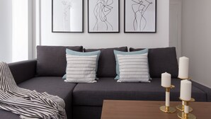 A modern living room with a grey sofa, striped cushions, and three framed abstract line drawings on the wall. - Park West by Allô Housing (London)