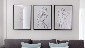 Three framed abstract artworks on a wall above a grey sofa with patterned cushions. - Park West by Allô Housing (London)