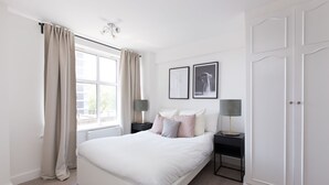 A bedroom with a large bed, two bedside tables with lamps, a wardrobe, and two framed pictures on the wall. - Park West by Allô Housing (London)