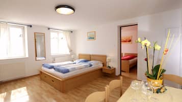 A bedroom with a wooden bed, bedside tables, a window with curtains, a small table with wine glasses, and a door leading to another room.