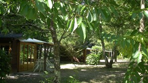 A wooden cabin with a covered porch and a small garden area. - Camping Le Petit Lion - Gites (Vendoire)
