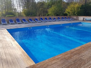 Piscina com água azul, cercada por um deck de madeira e espreguiçadeiras azuis.