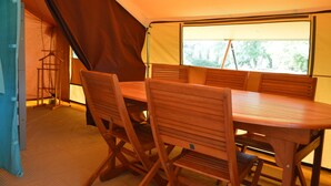Une pièce aménagée avec une tente, une table et des chaises en bois, un portant à vêtements et une fenêtre donnant sur la forêt.