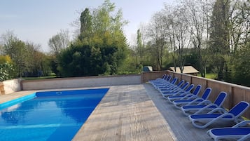 A swimming pool with a wooden deck and lounge chairs.