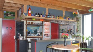 Un espace bar avec des étagères remplies de bouteilles, un réfrigérateur, un tableau noir servant de menu et une petite table avec des chaises.