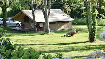 A tented accommodation with a car parked nearby, surrounded by greenery.