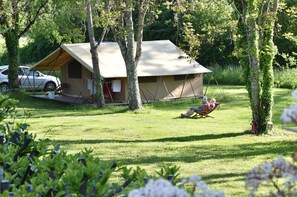 A tented accommodation with a car parked nearby, surrounded by greenery. - Camping Le Petit Lion - Tente Safari (Vendoire)