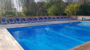 Une piscine à l’eau bleue, entourée d’une terrasse en bois et de chaises longues bleues.