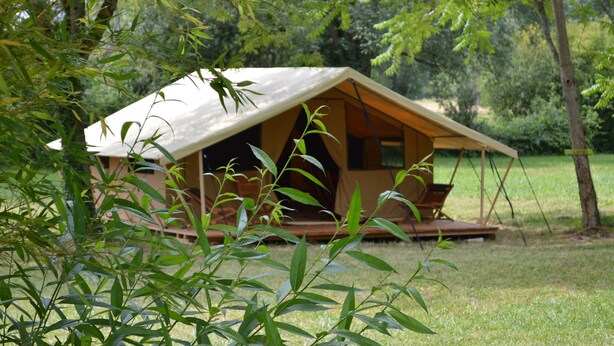 Une petite cabane en bois à un seul étage, de forme triangulaire, dotée d’un porche et entourée d’une végétation luxuriante.