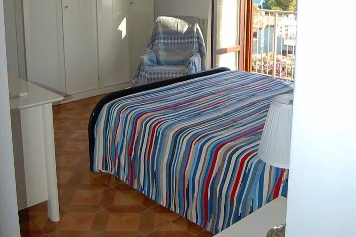 A bedroom with a bed, a chair, a wardrobe, and a balcony with a view.