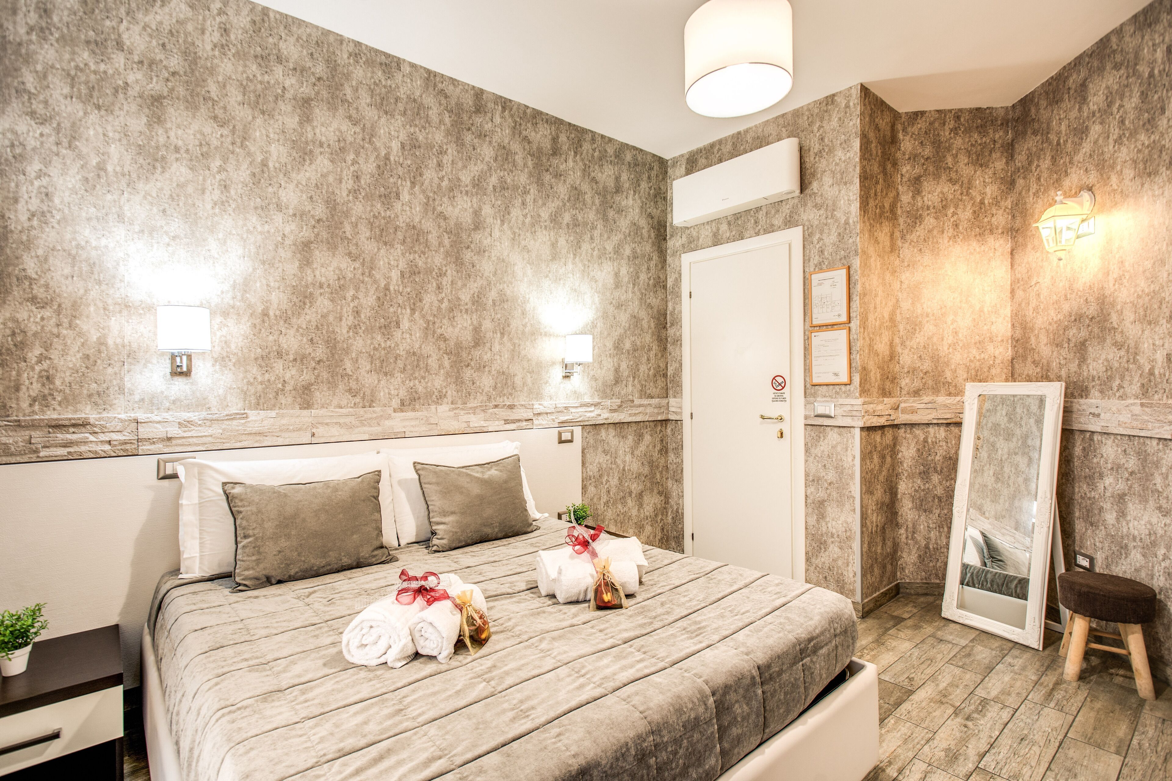 A hotel room with a large bed, a nightstand, a small stool, a mirror, and a door.