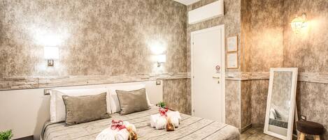 A hotel room with a large bed, a nightstand, a small stool, a mirror, and a door.