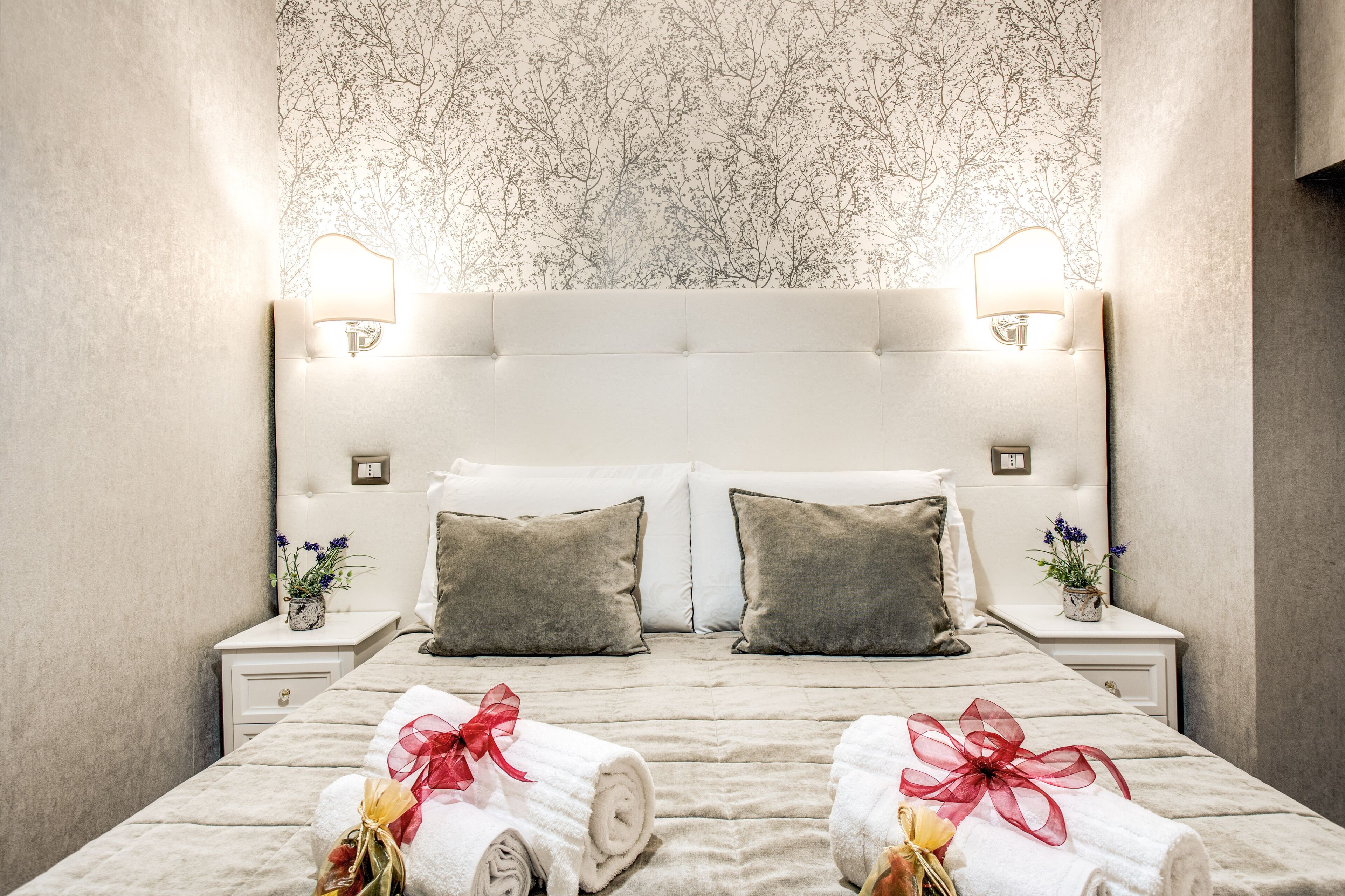 A neatly made bed with two pillows, a nightstand with a lamp, and a floral wallpaper.