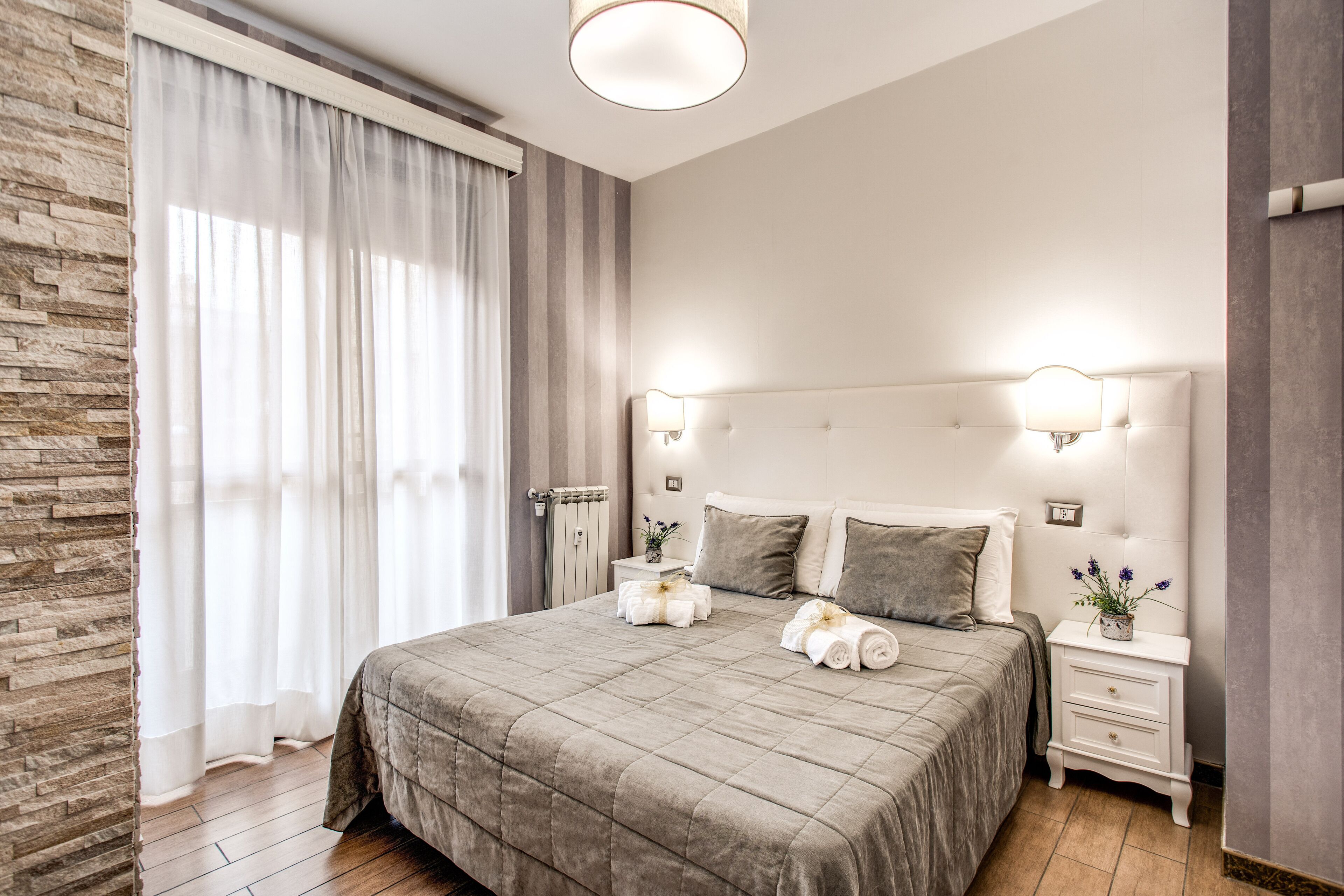 A neatly arranged bedroom with a large bed, a nightstand, and a wall-mounted lamp.