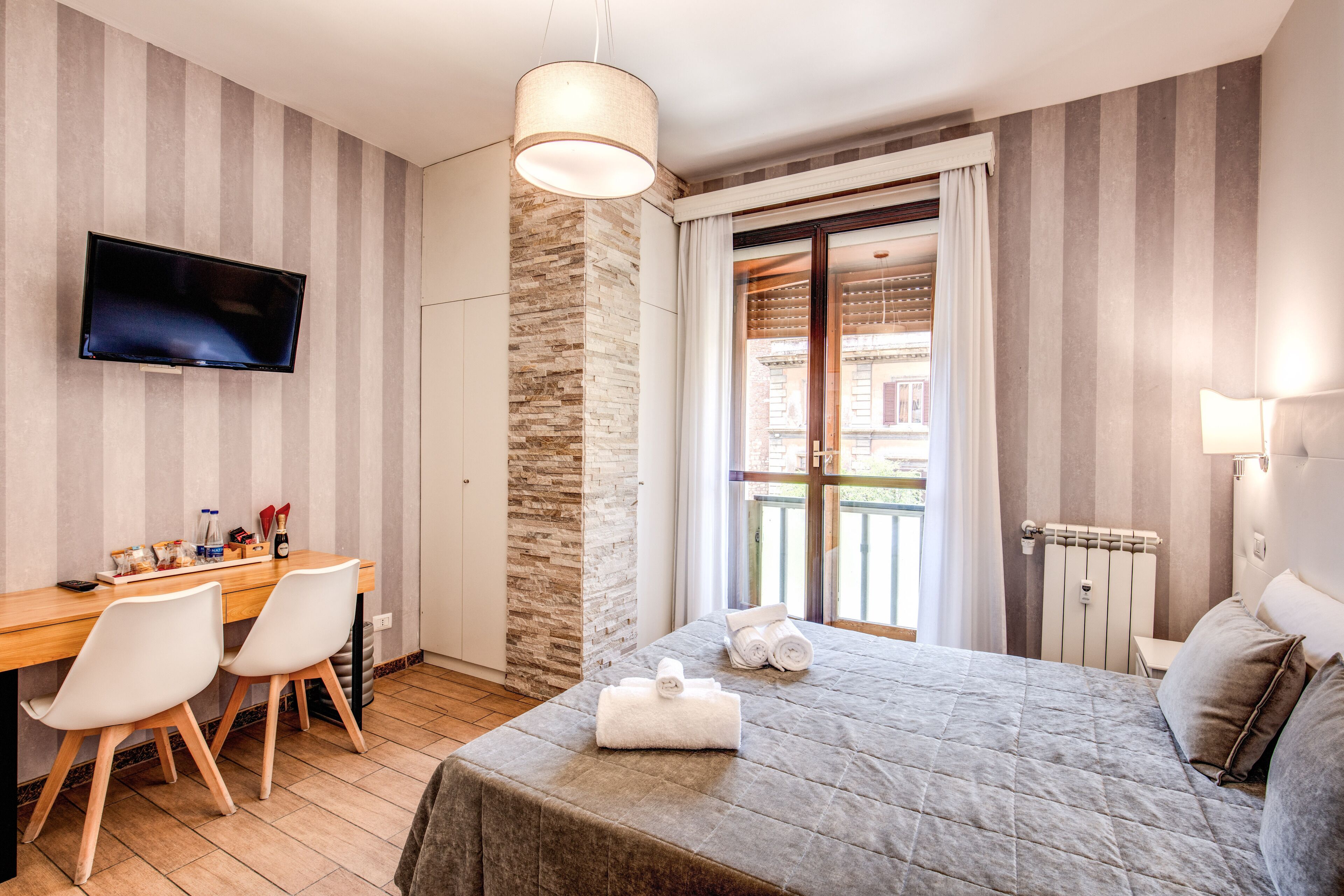 A hotel room with a bed, a desk with chairs, a television, and a window with curtains.