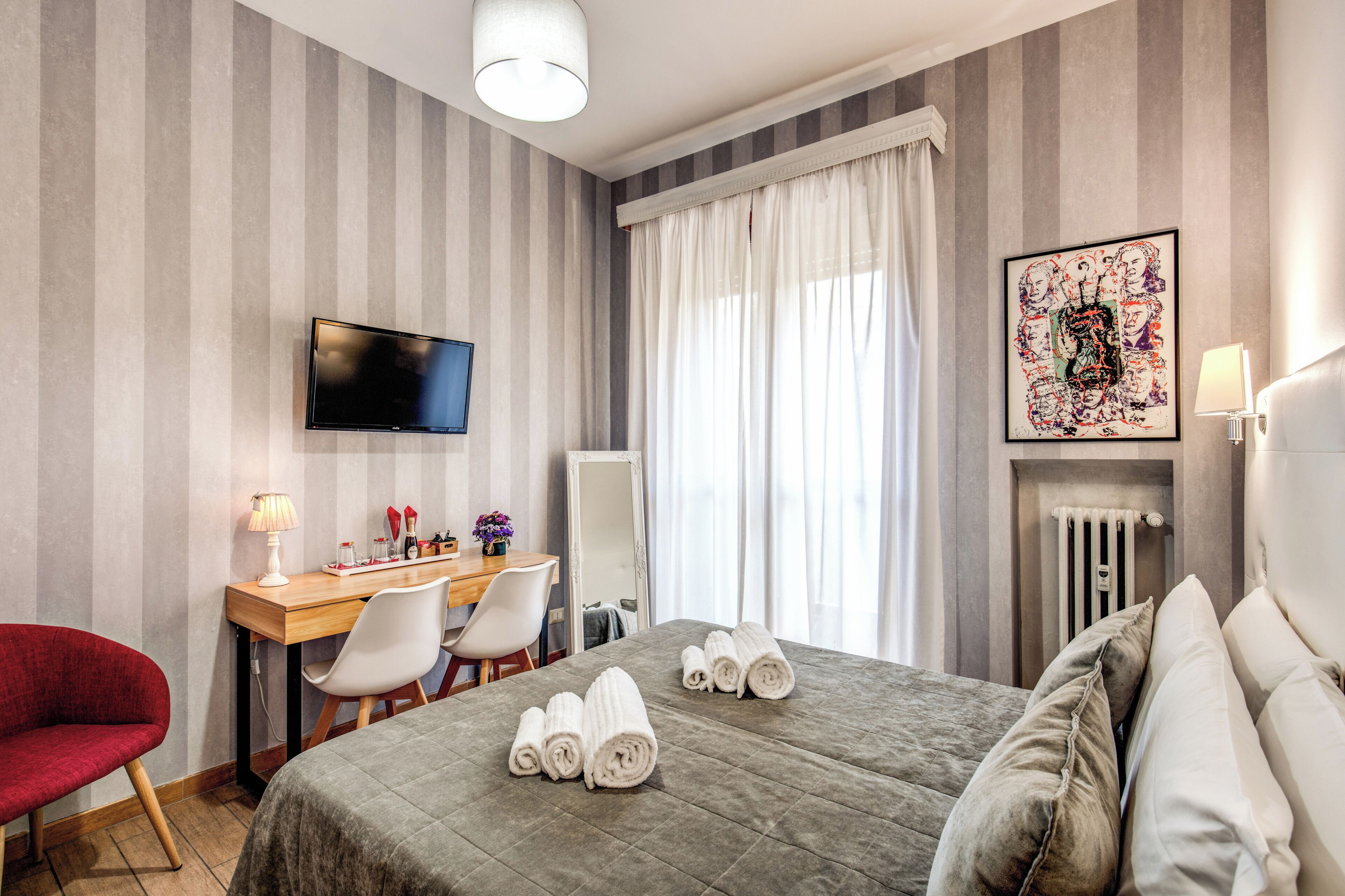 A hotel room with a bed, a desk with a chair, a television, and a radiator.