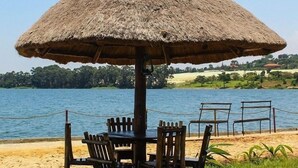 A thatched umbrella table with chairs, overlooking a body of water. - Nyange Resort and Marina (Entebbe)