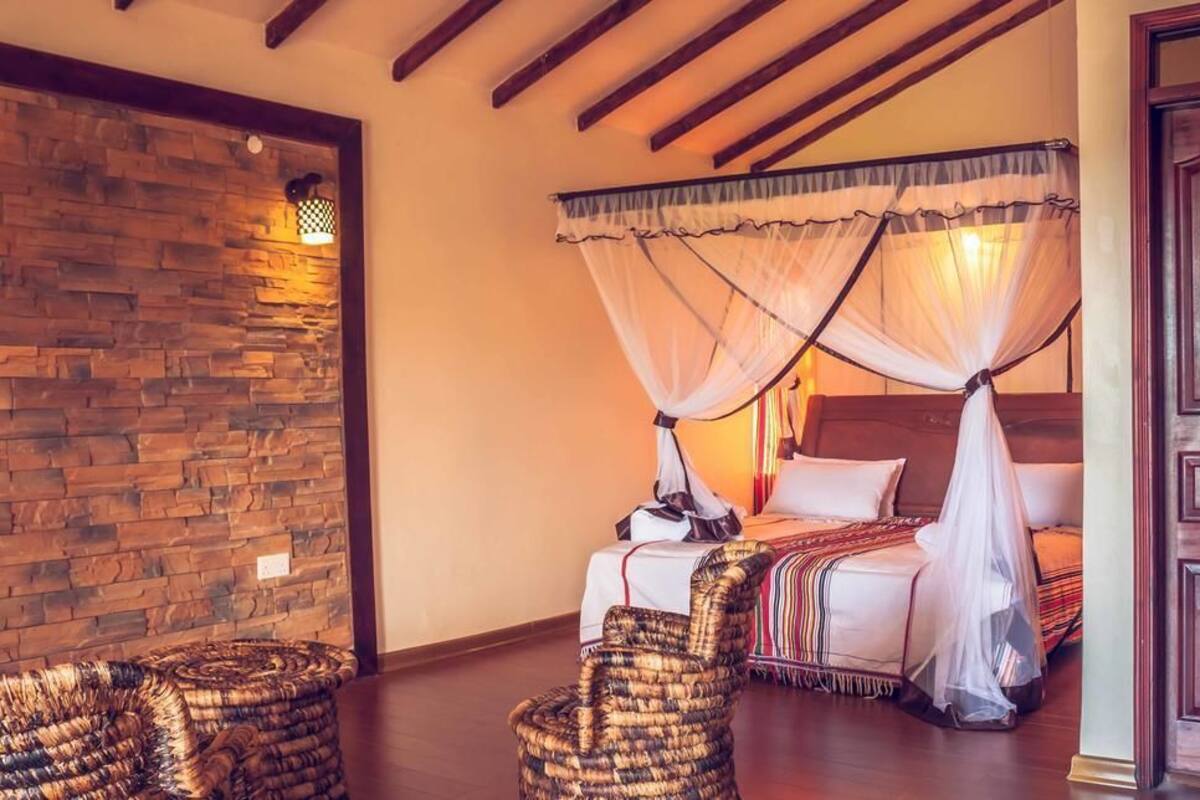 A bedroom with a stone wall, a canopy bed, wicker chairs, and a wooden door.