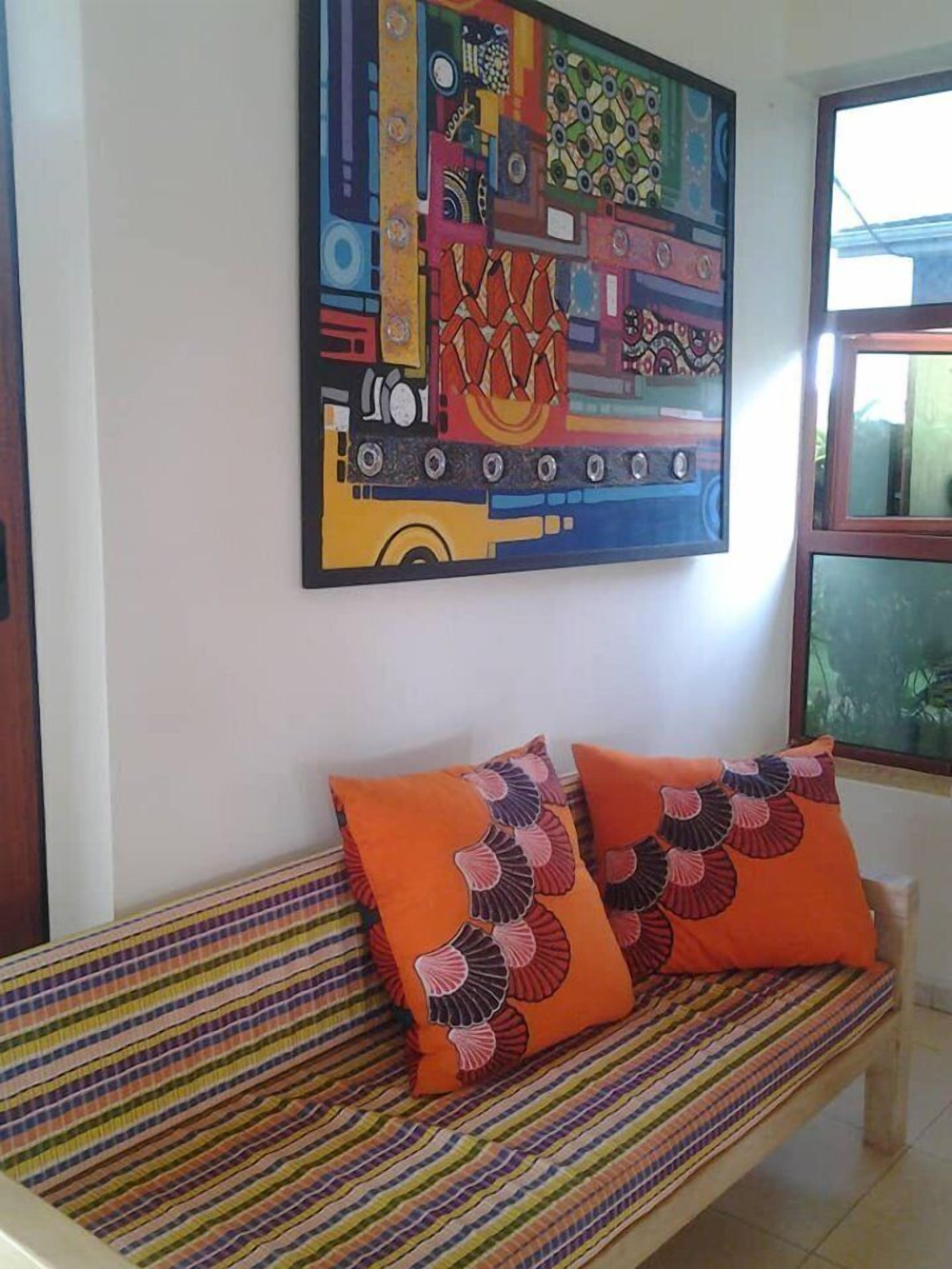 A room with a colorful striped sofa, a vibrant abstract painting on the wall, and a window with a view of greenery.