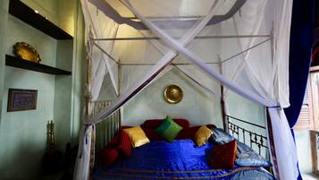 A bed with a canopy, a brass plate on the wall, and a shelf with a decorative item.