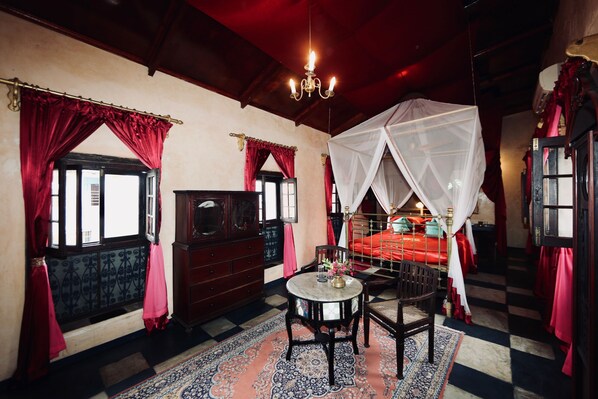 A traditional room with a bed under a canopy, a wooden dresser, a table with chairs, and a patterned rug. - Emerson on Hurumzi (Zanzibar Town)