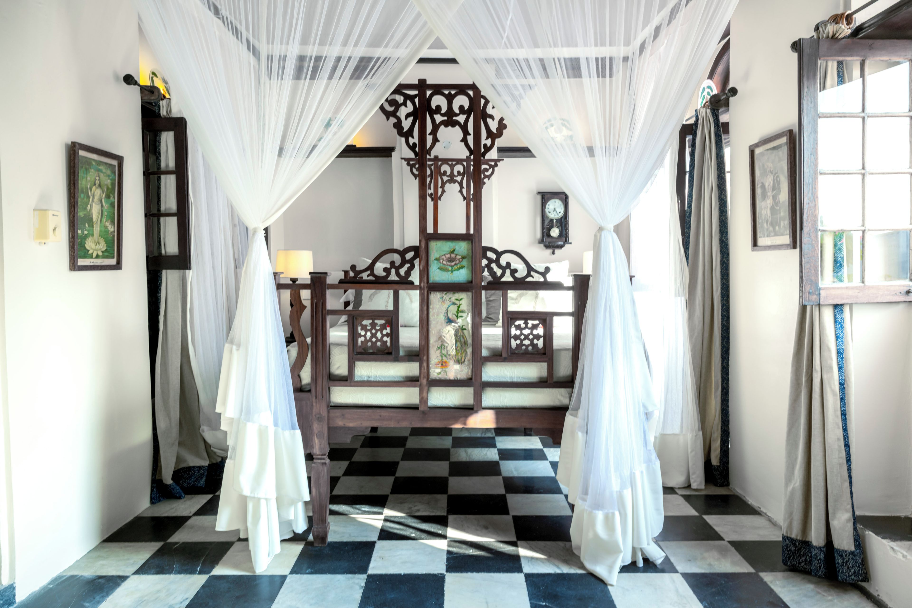 A checkered floor leading to a bed with a canopy, a clock on the wall, and a framed picture on the wall.