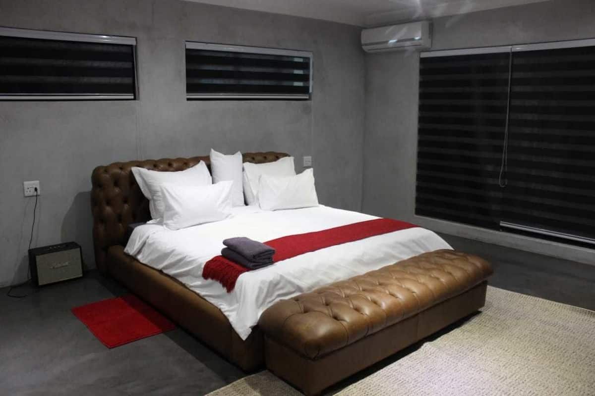 Une chambre à coucher moderne avec un grand lit, un plaid rouge et un pouf en cuir.