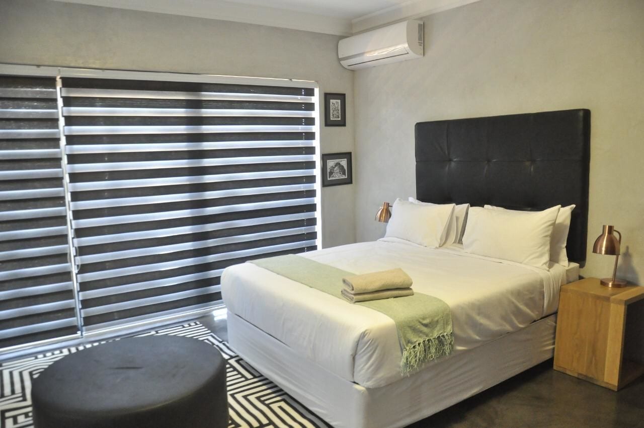 A hotel room with a large bed, a bedside table with a lamp, and a window with horizontal blinds.