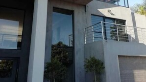 Een modern gebouw met een plat dak, grote ramen en een betonnen gevel. Voor de ingang staan twee plantenbakken met planten.